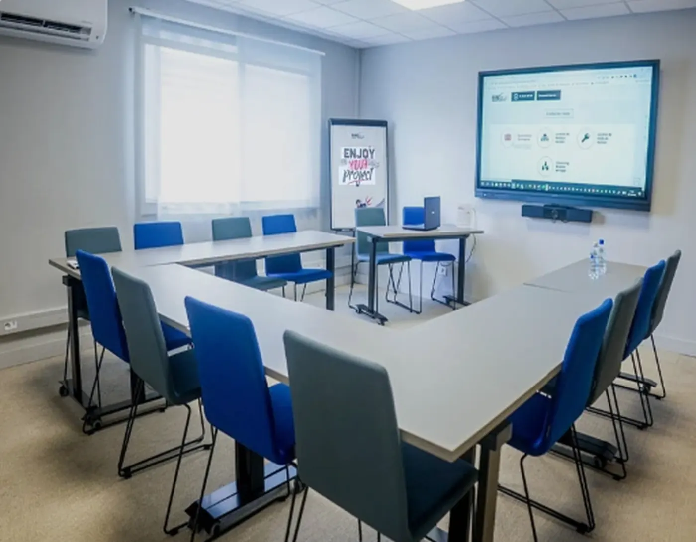 Salle de formation avec tables en U, douze chaises et écran interactif